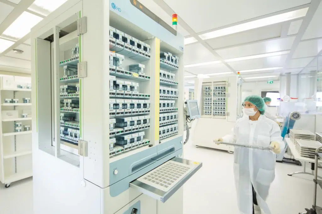 Mitarbeiterin von Multidos in Schutzkleidung bestückt den Blisterautomaten mit einem neuen Tablett – moderne und hygienische Arzneimittelverblisterung für die Gondermann Apotheken