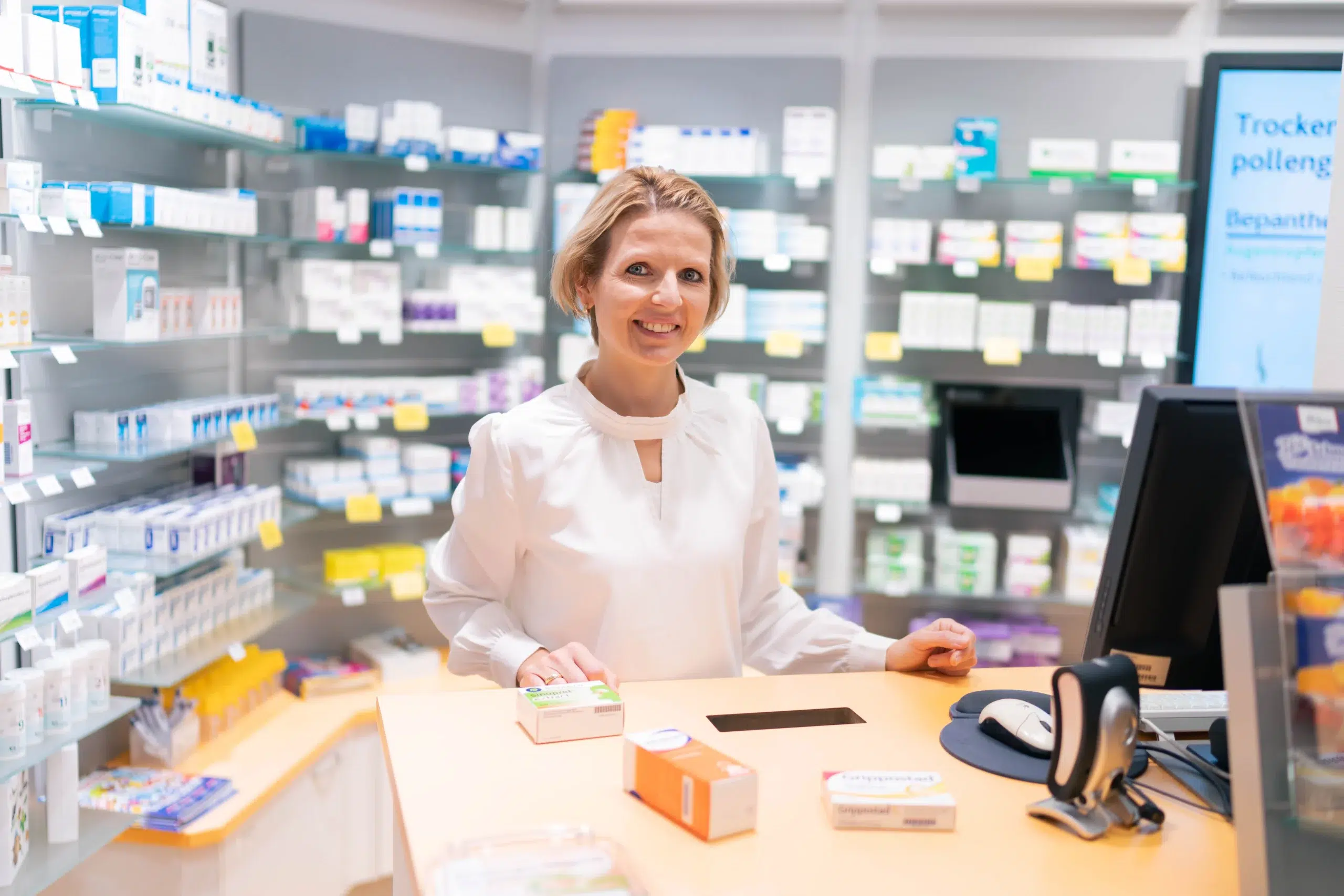 Eine Apothekerin der Gondermann Apotheken steht lächelnd an der Kasse. Auf dem Tresen vor ihr liegen verschiedene Medikamentenpackungen – ein Moment, der die persönliche und kompetente Beratung in der Apotheke widerspiegelt.
