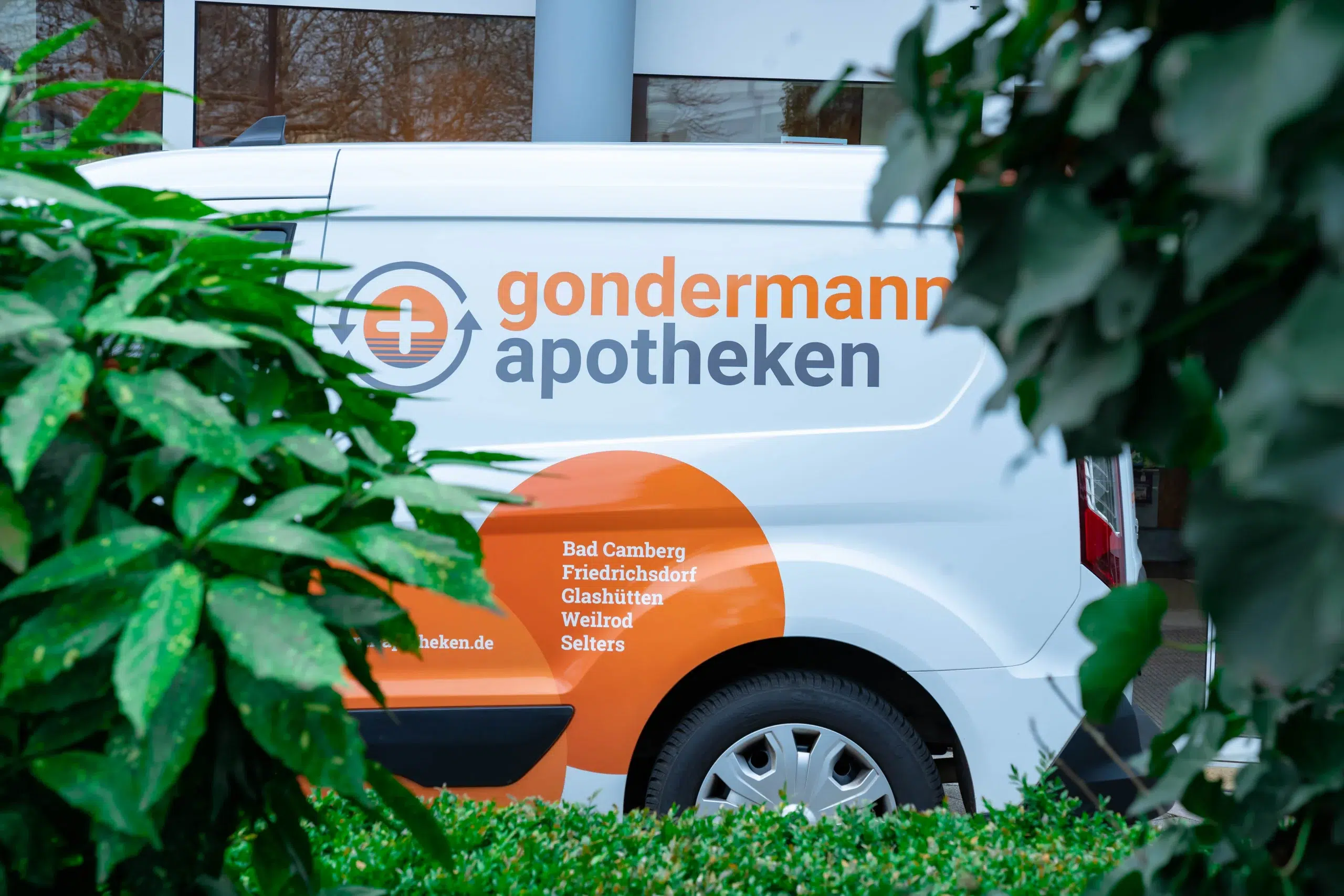 Detailaufnahme eines Botendienstfahrzeugs der Gondermann Apotheken, eingebettet in frisches Grün. Nur ein Teil des Fahrzeugs ist sichtbar – ein stimmungsvolles Bild, das die Nähe zur Natur und den zuverlässigen Lieferservice der Apotheke unterstreicht.