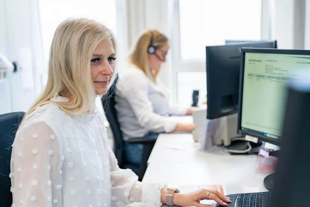 Büroszene aus der Heimversorgung: Zwei Mitarbeiterinnen sitzen am PC und koordinieren digitale Versorgungsabläufe für pflegebedürftige Patientinnen und Patienten – moderne Organisation bei Gondermann Apotheken