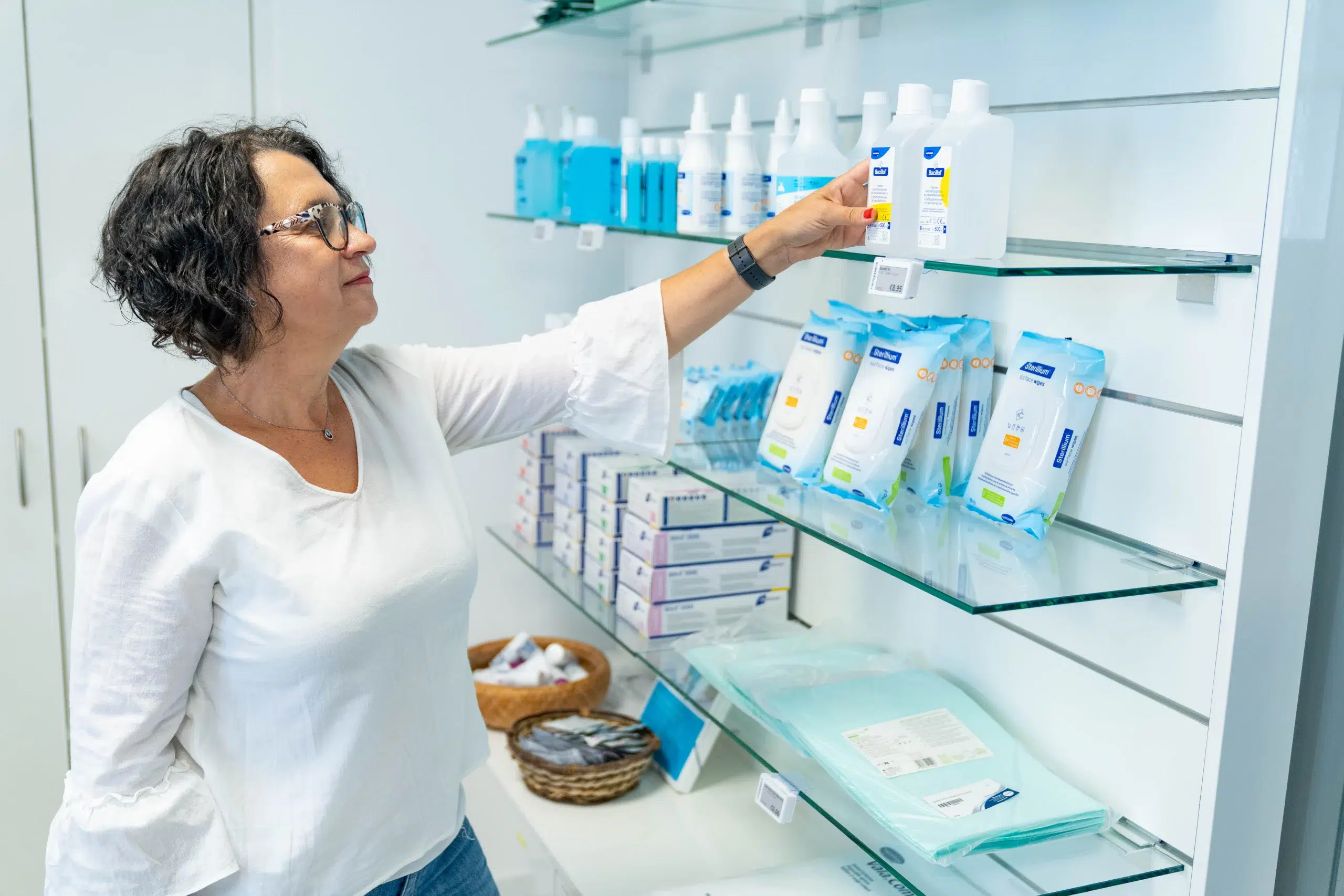 Mitarbeiterin im Oranienpflegeshop greift ins Regal mit Desinfektionsmitteln und Pflegehilfsmitteln – echte Momentaufnahme aus dem Arbeitsalltag in der Versorgung pflegebedürftiger Menschen