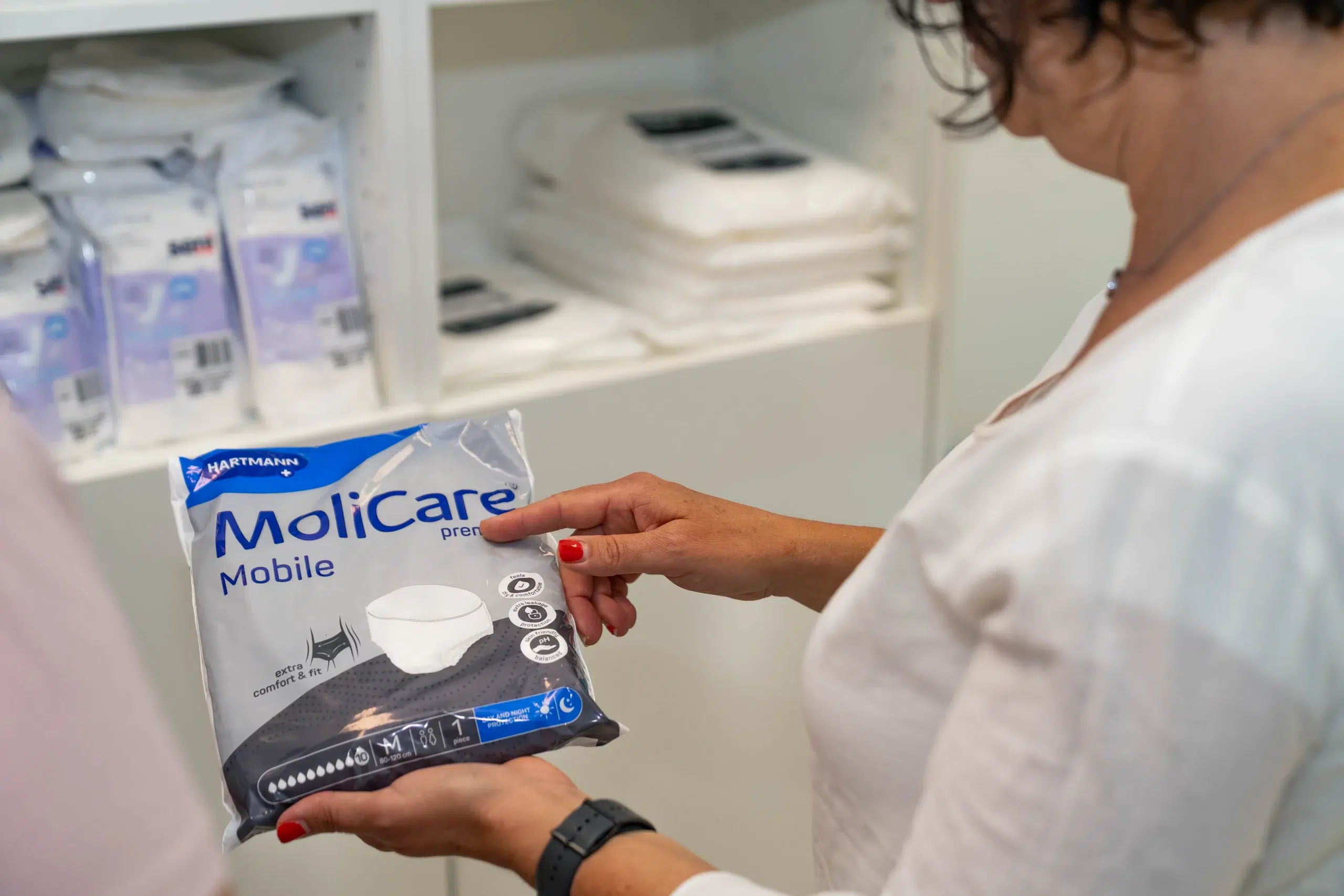 Detailaufnahme eines Inkontinenzprodukts, das von einer Mitarbeiterin des OranienPflegeShops diskret einer Kundin gezeigt wird. Die Verpackung liegt gut sichtbar in ihren Händen – ein Moment, der die sensible und fachkundige Beratung im Pflegebereich unterstreicht.