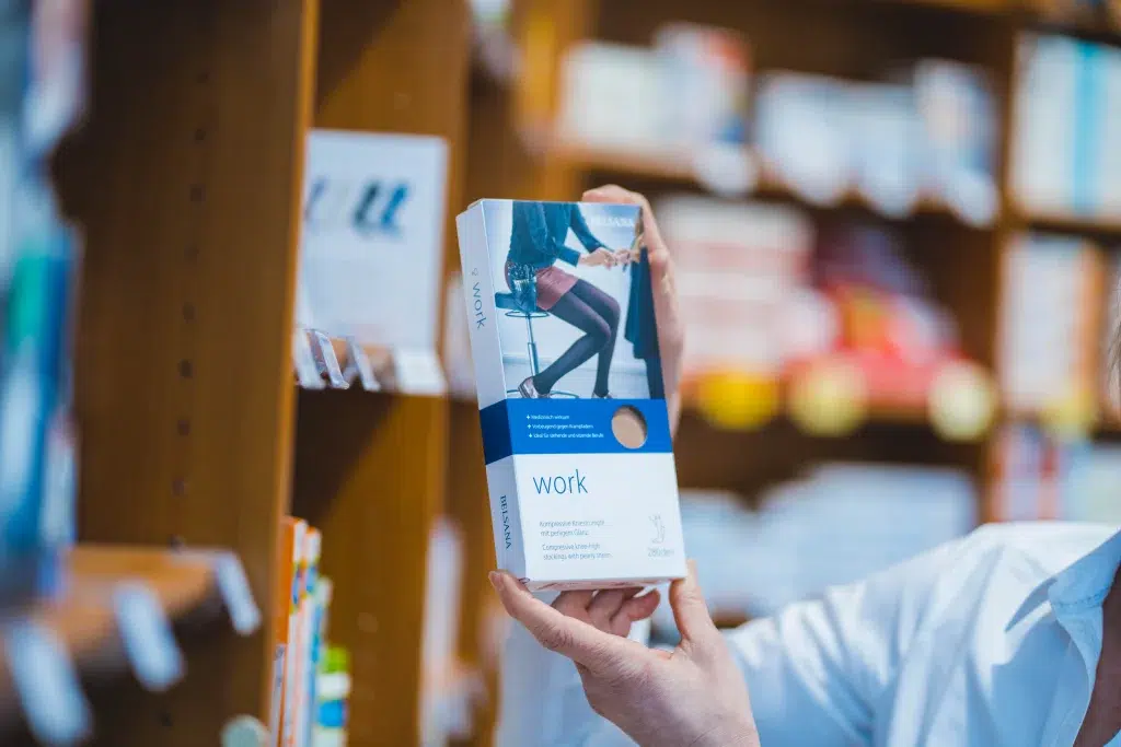 Detailaufnahme: Mitarbeiterin der Gondermann Apotheken hält eine Packung Kompressionsstrümpfe in die Kamera – hochwertige medizinische Versorgung für Venenunterstützung und individuelle Beratung