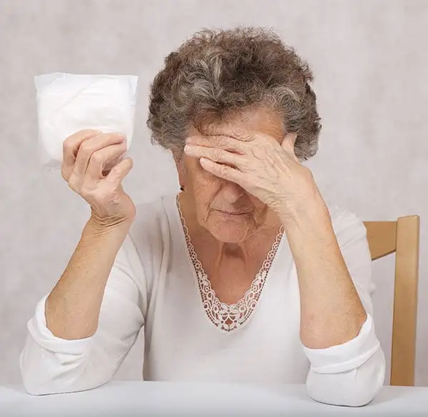 Symbolbild für das sensible Thema Inkontinenz: Eine ältere Dame hält sich die Hand vors Gesicht und zeigt in der anderen Hand eine Einlage – Ausdruck von Scham und Offenheit im Umgang mit einem oft tabuisierten Pflegebedürfnis