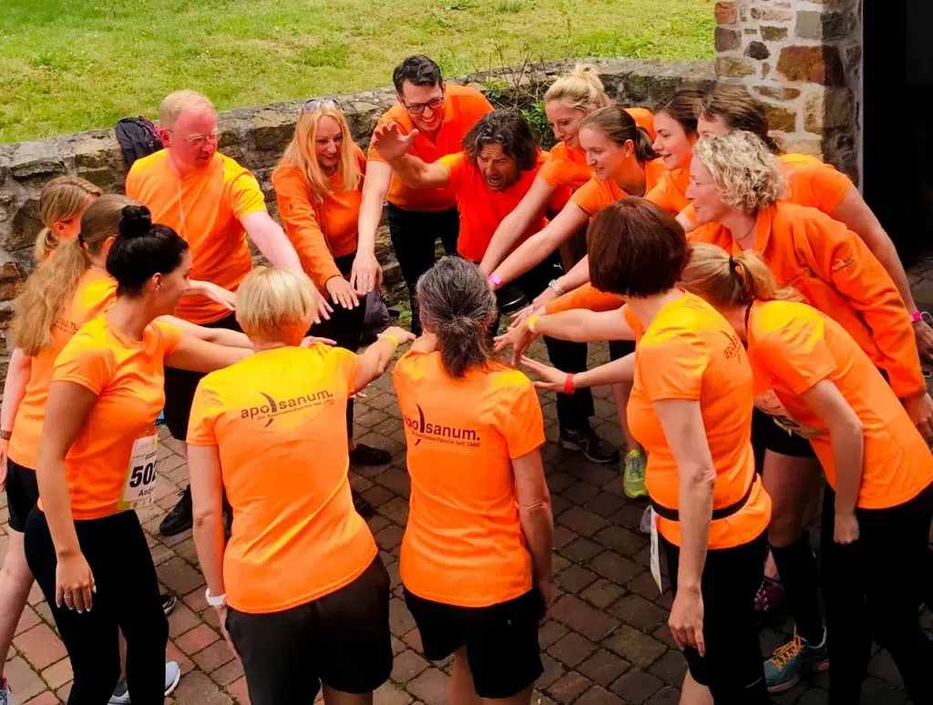 Team der Gondermann Apotheken in orangefarbenen Shirts vereint die Hände im Kreis – Symbol für Zusammenhalt, Engagement und gelebten Teamgeist in Ihrer Apotheke vor Ort.